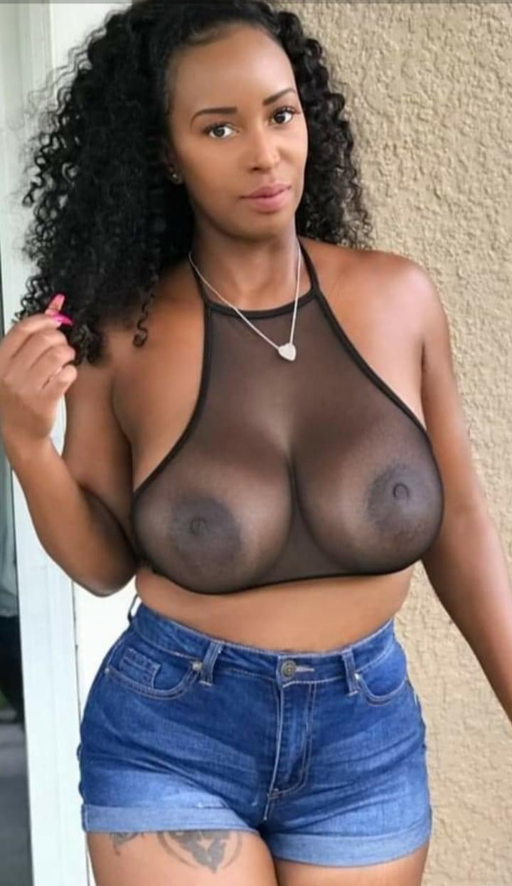 Curly black girl wearing a blouse sheer enough to show off her large, full breasts with dark nipples